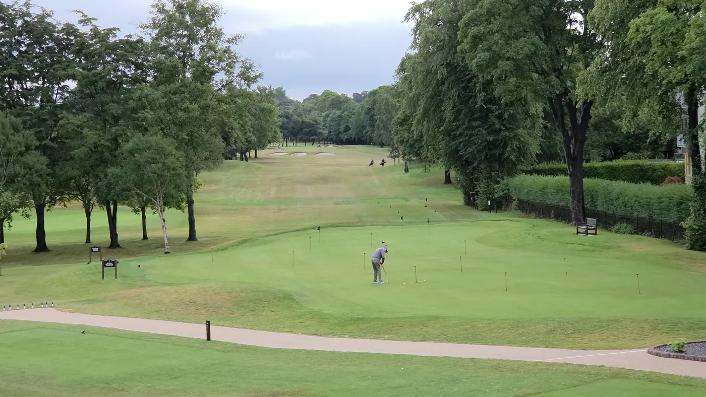 A golf hole framed by mature trees, closely mown turf running away from the camera