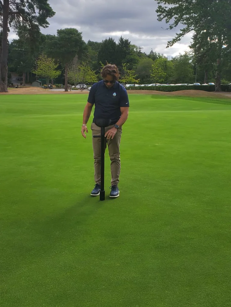 A turf professional taking a TOMi reading on a championship putting green, mature pines behind