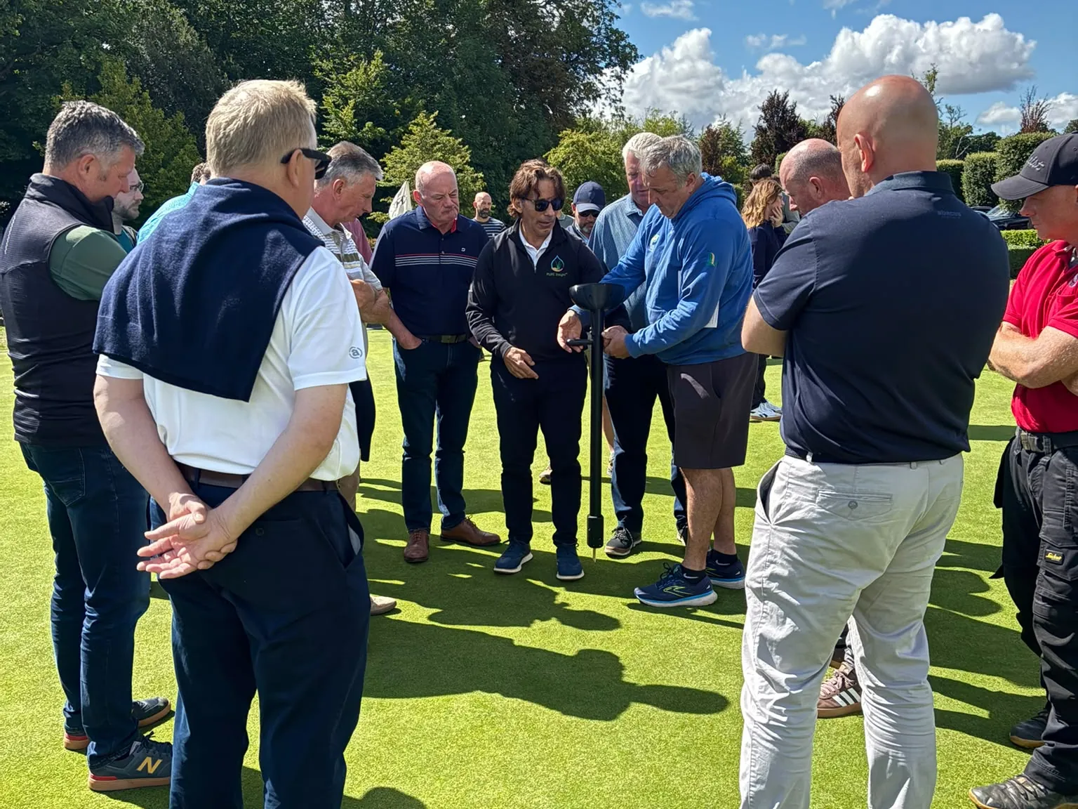 Turf managers gathered around Carmen Magro and a TOMi instrument on a putting green during a demonstration