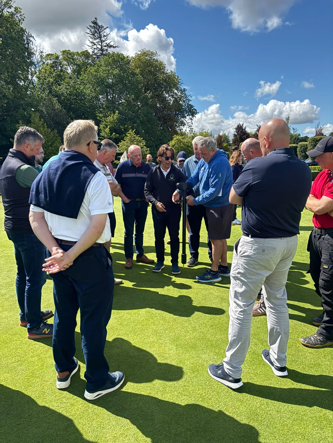 Carmen Magro demonstrating the TOMi instrument to a circle of turf managers on a putting green