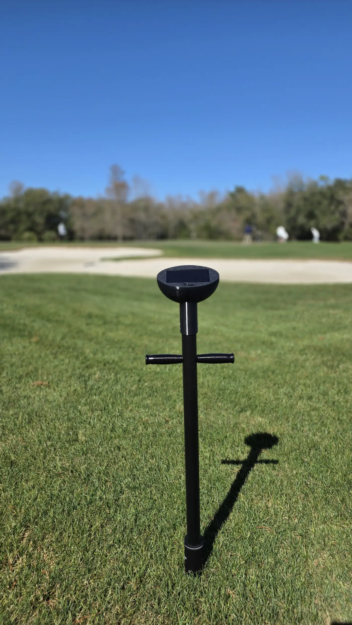A TOMi instrument standing upright in a putting green, bunker and treeline behind